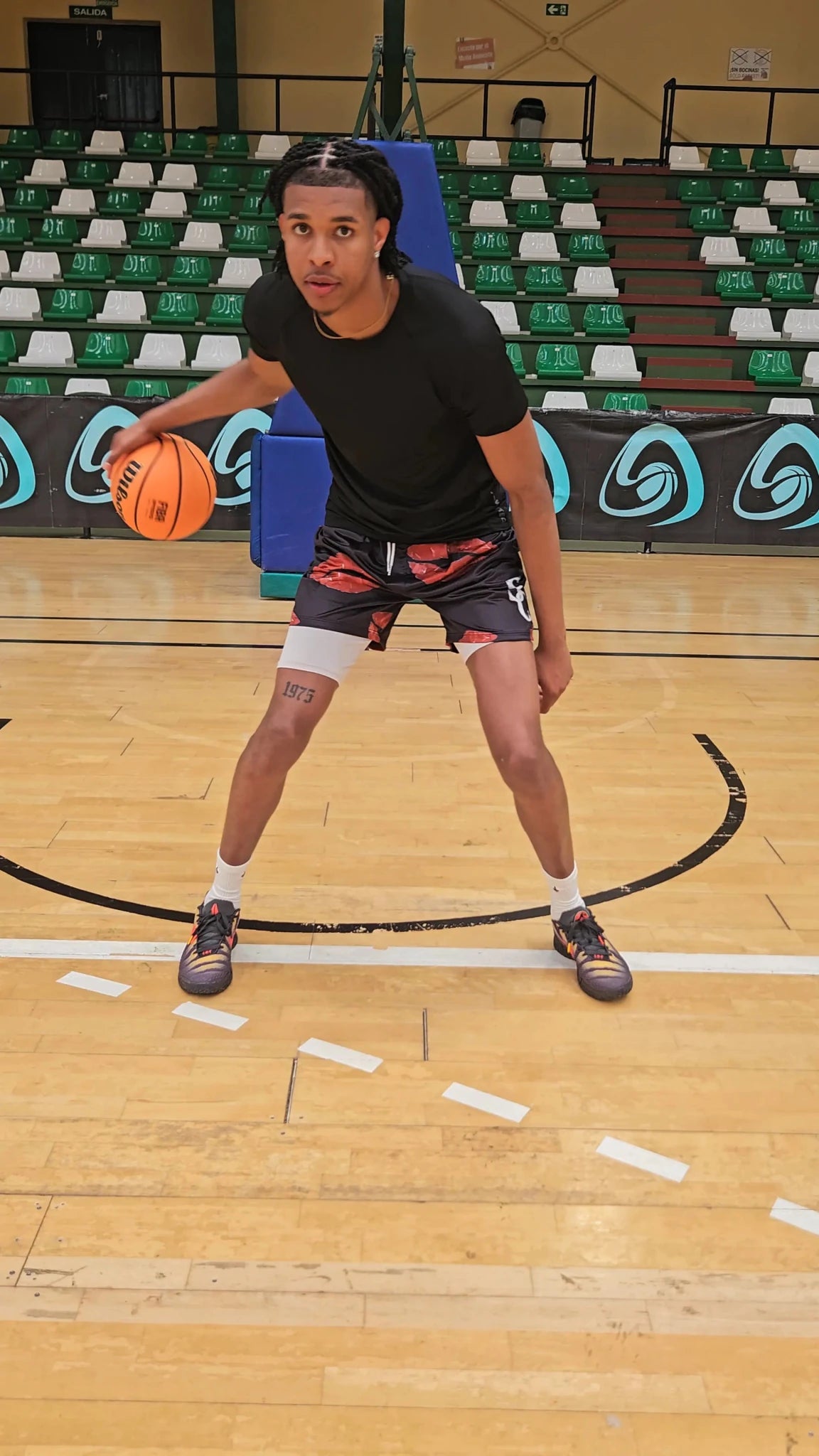 SwishGang player in dribbling stance wearing Kisses basketball shorts and black tee on indoor hardwood court