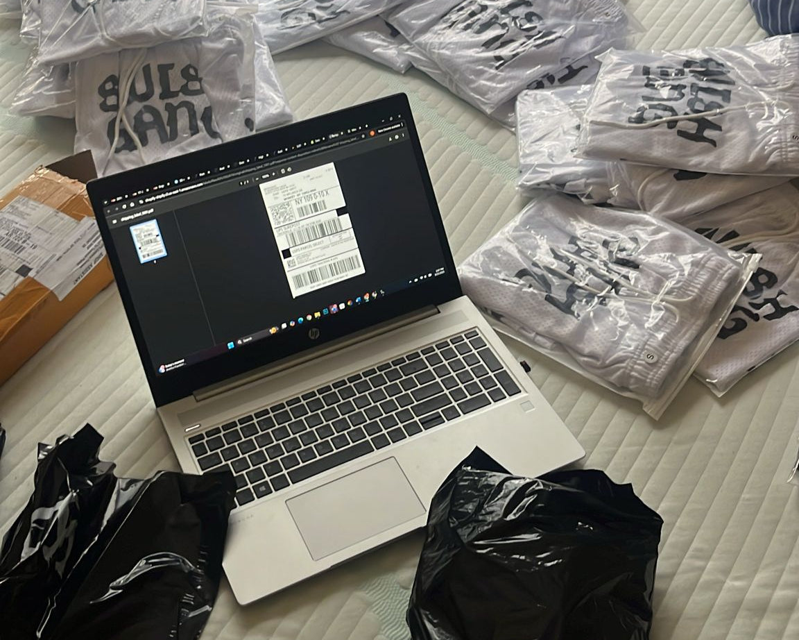 SwishGang founder showing his laptop generating a shipping label while preparing basketball shorts orders