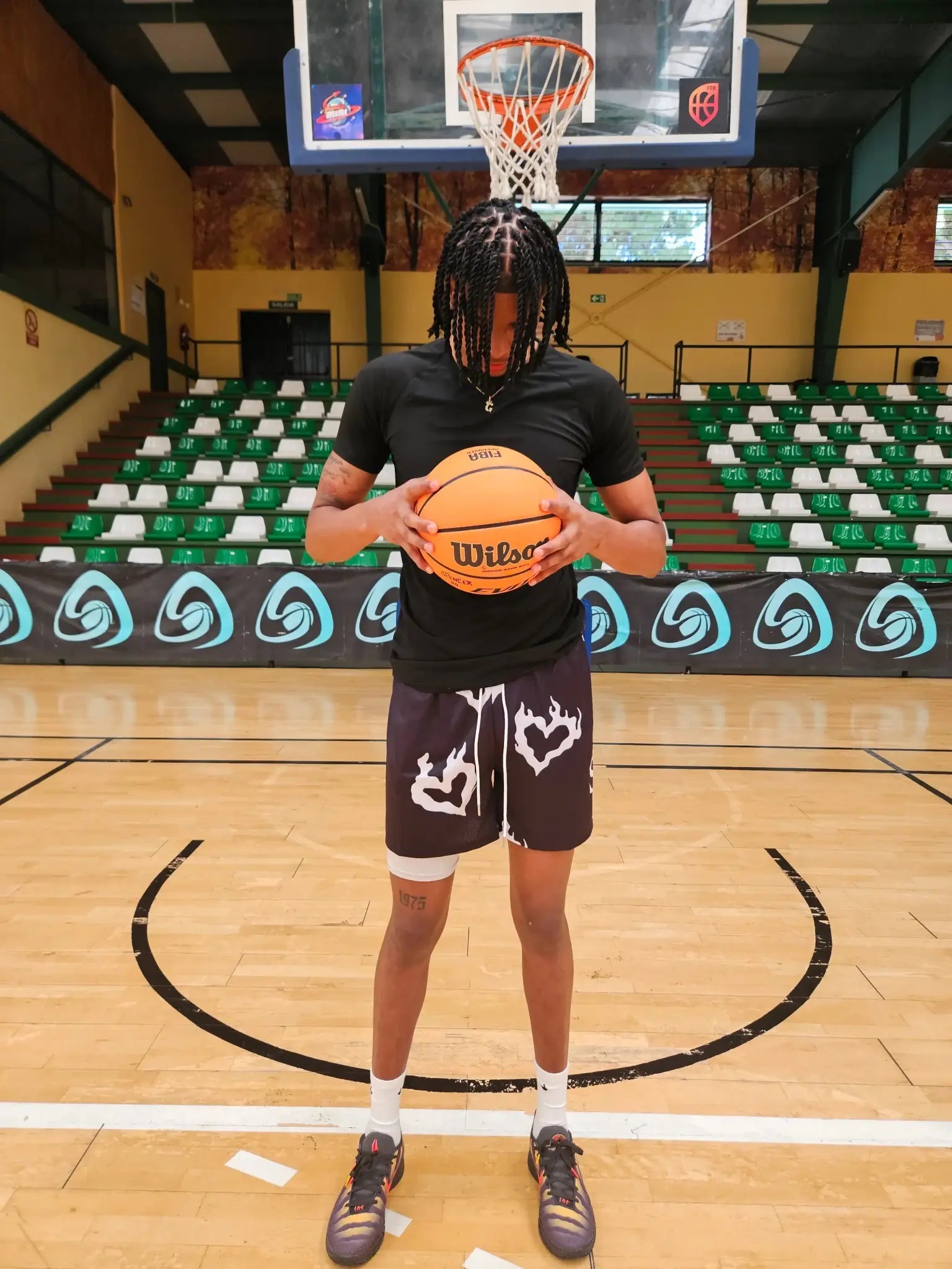 Full body shot of SwishGang model in black flaming heart basketball shorts, standing on court holding basketball