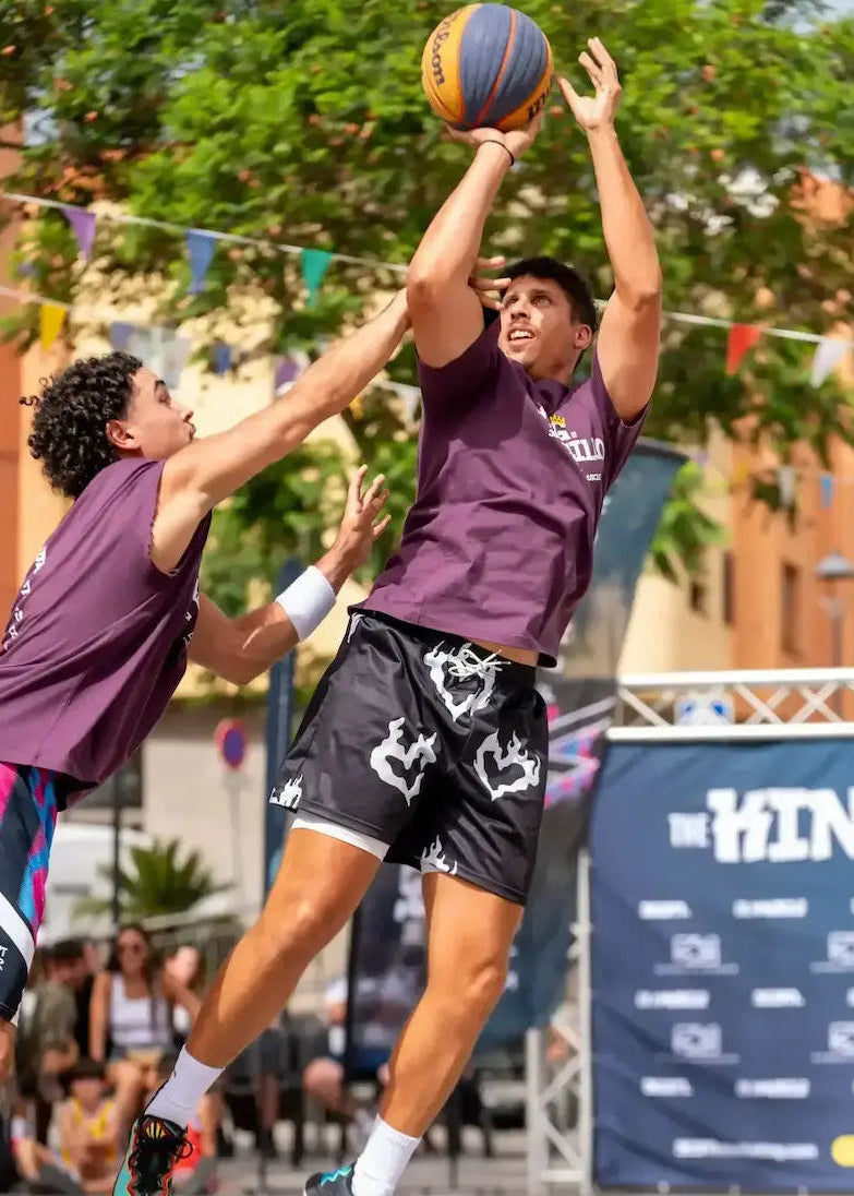 Action shot of a basketball player wearing black shorts with white prints during an outdoor street basketball tournament match.