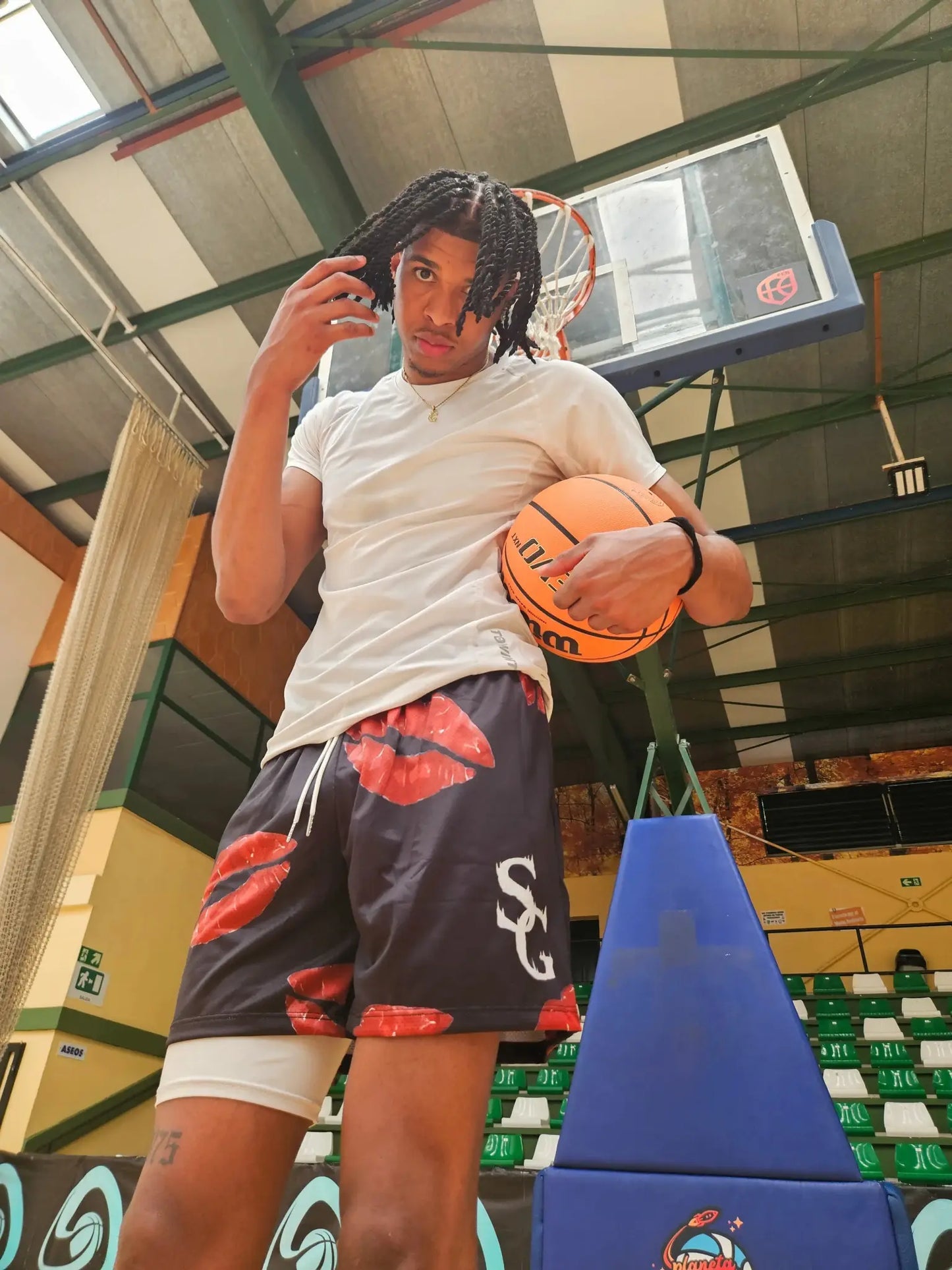 SwishGang model wearing black basketball shorts with red kiss print, holding basketball on court