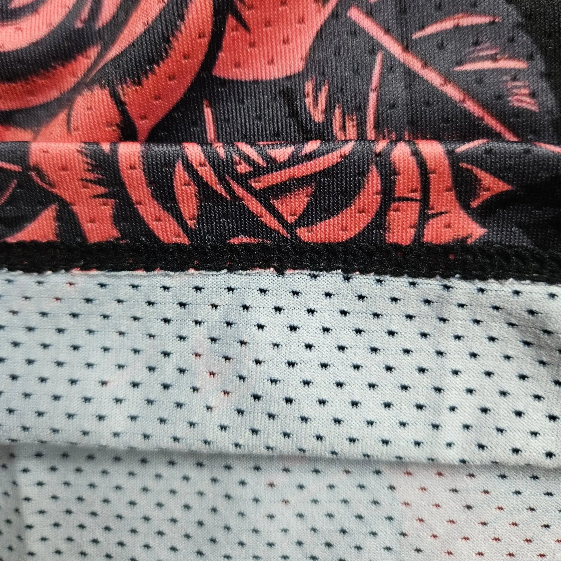 Close-up detail shot showing the mesh fabric texture and hem of the black and red rose-print basketball shorts