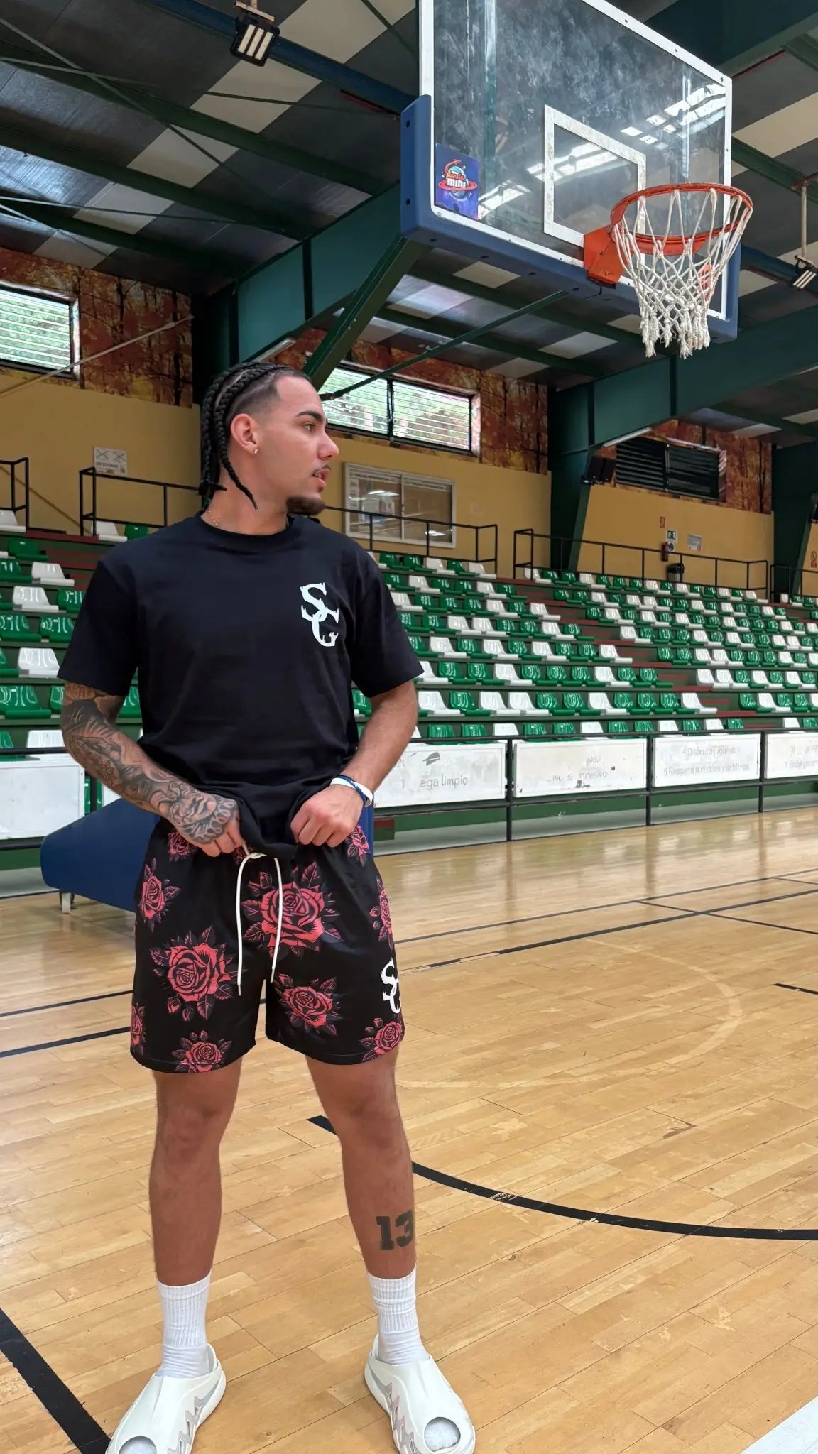 Basketball player wearing black basketball shorts with a red rose pattern and a matching black t-shirt, standing on an indoor basketball court