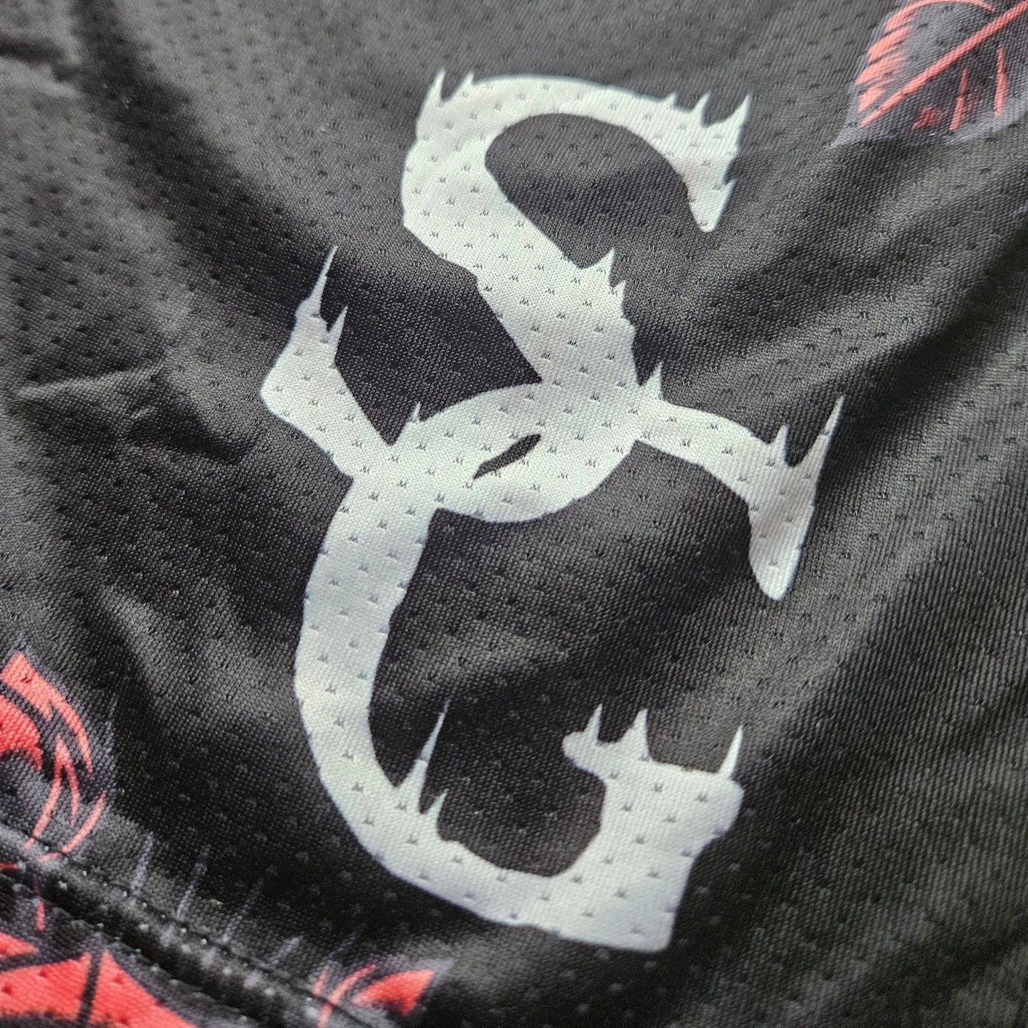 Close-up detail of the white logo printed on black basketball shorts with a red rose pattern