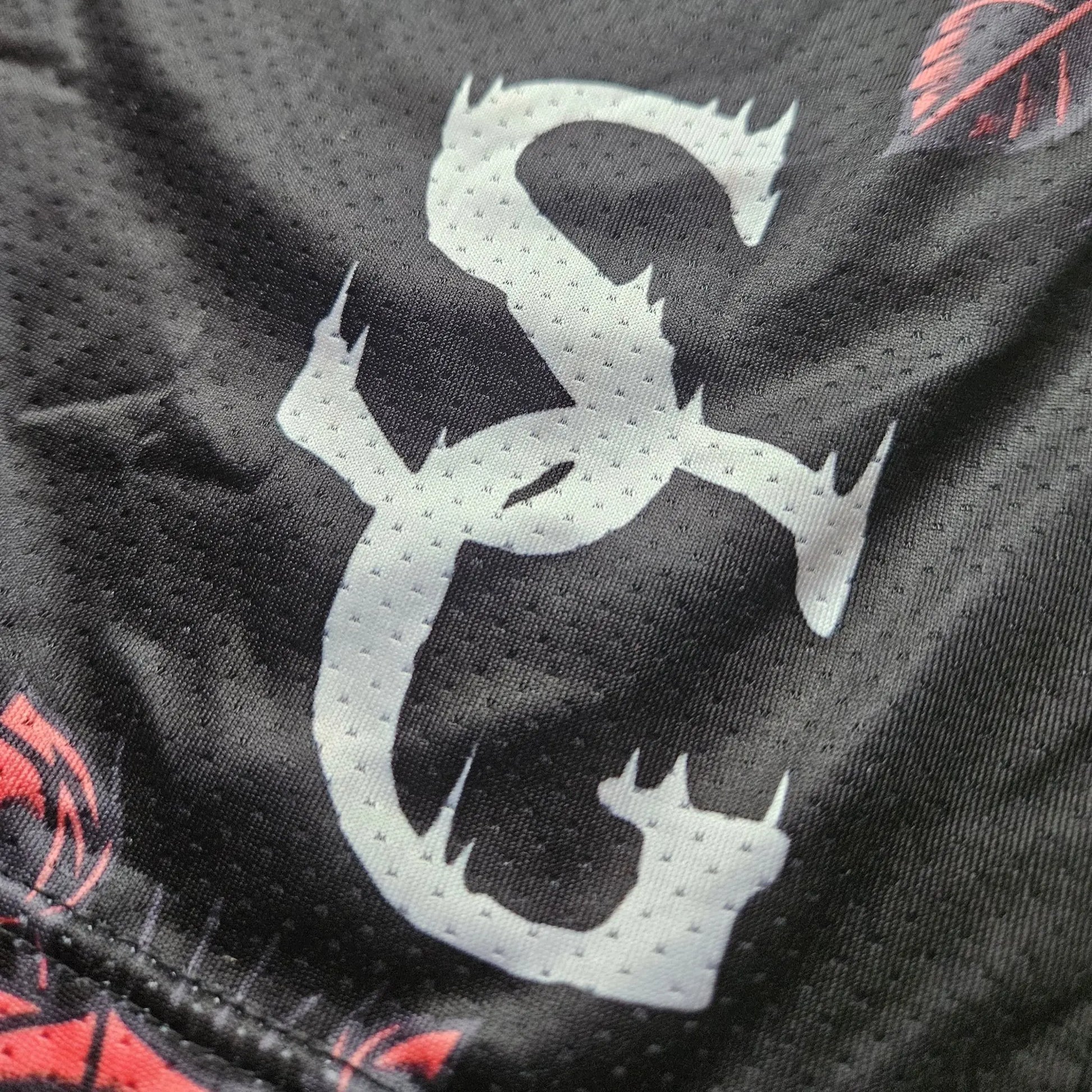 Close-up detail of the white logo printed on black basketball shorts with a red rose pattern