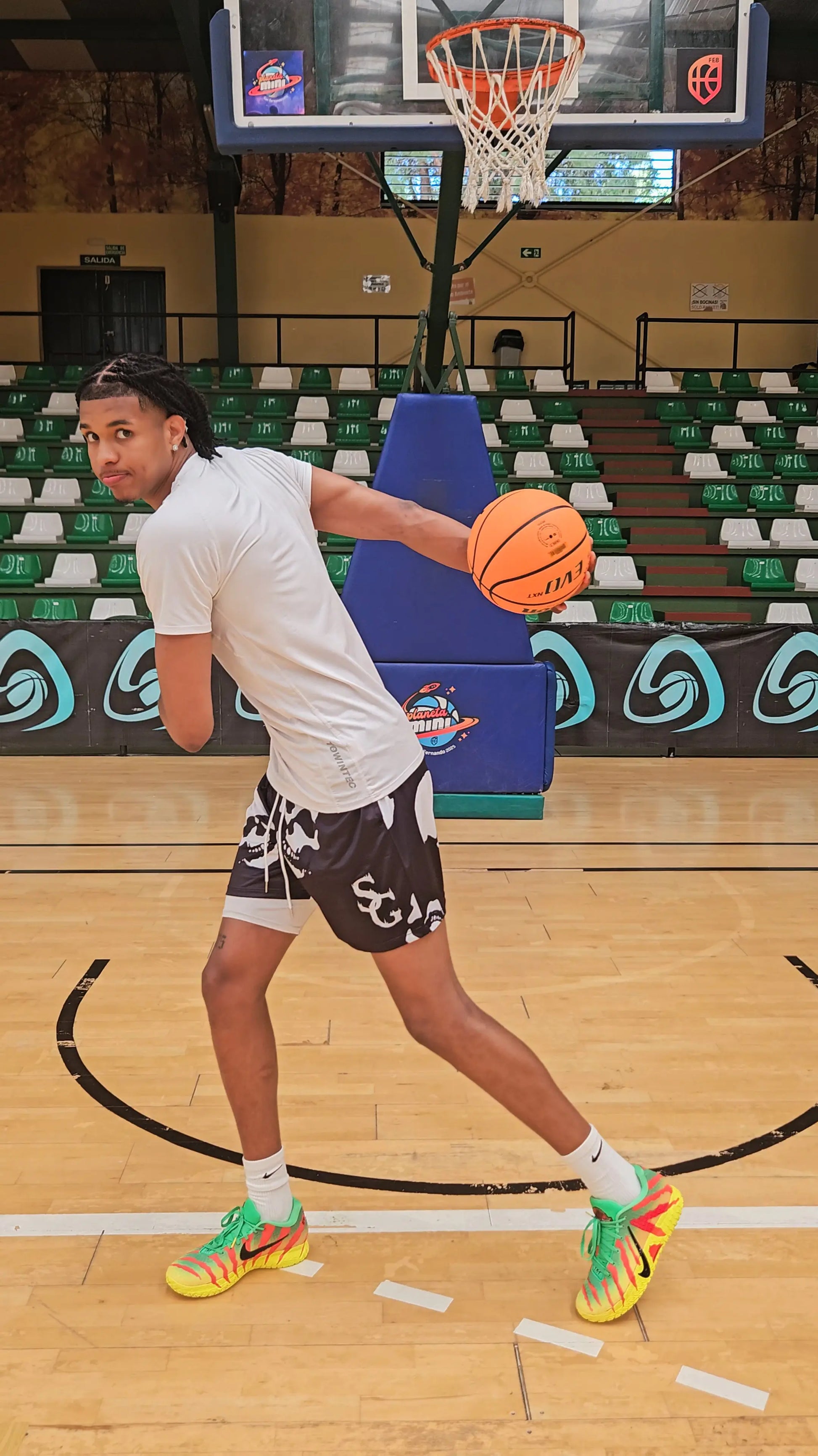 Action shot of a basketball player turning with a basketball on an indoor court, wearing black basketball shorts with a white skull pattern