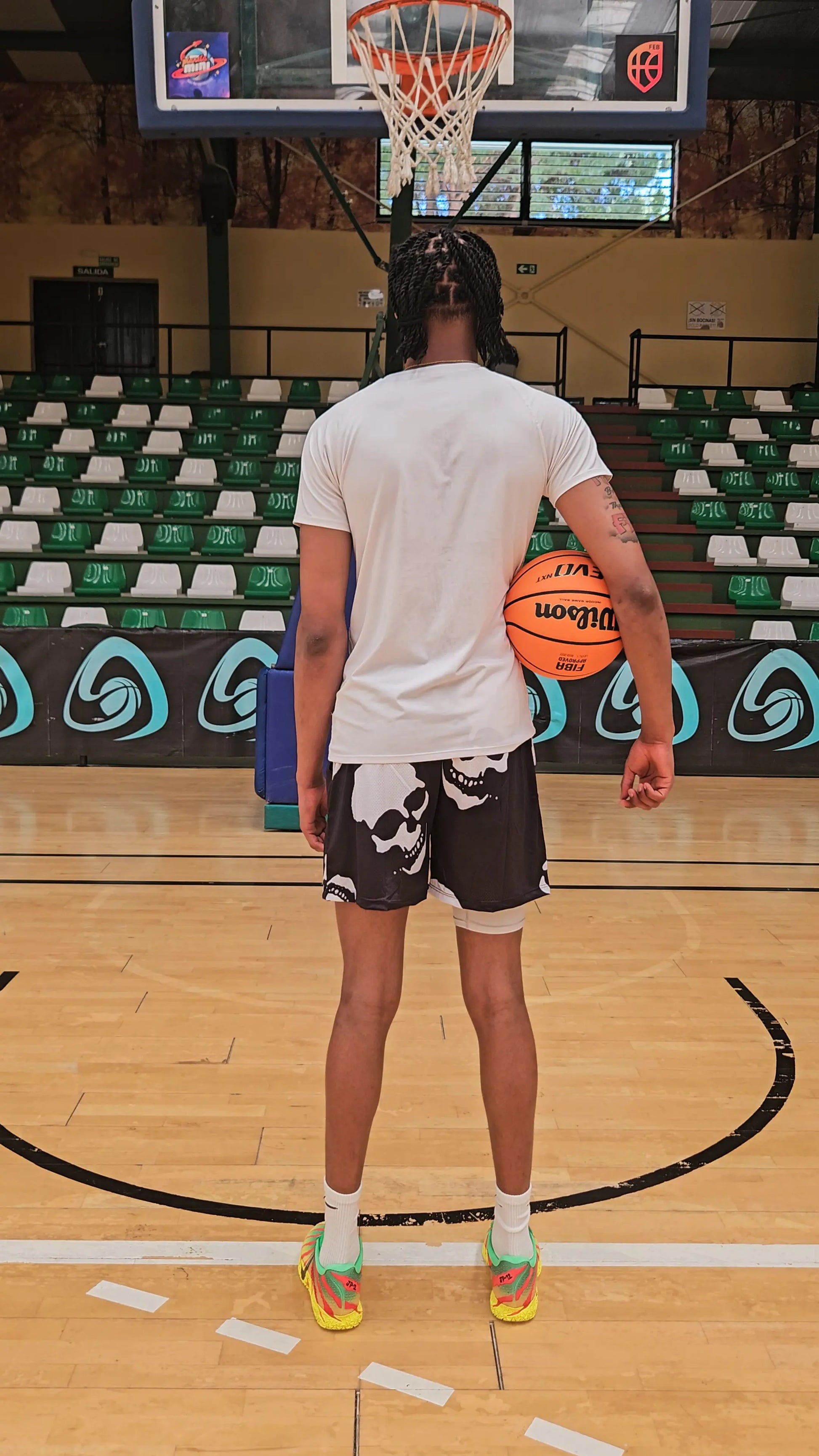 Back view of a basketball player wearing black basketball shorts with a white skull pattern, standing on a court holding a basketball