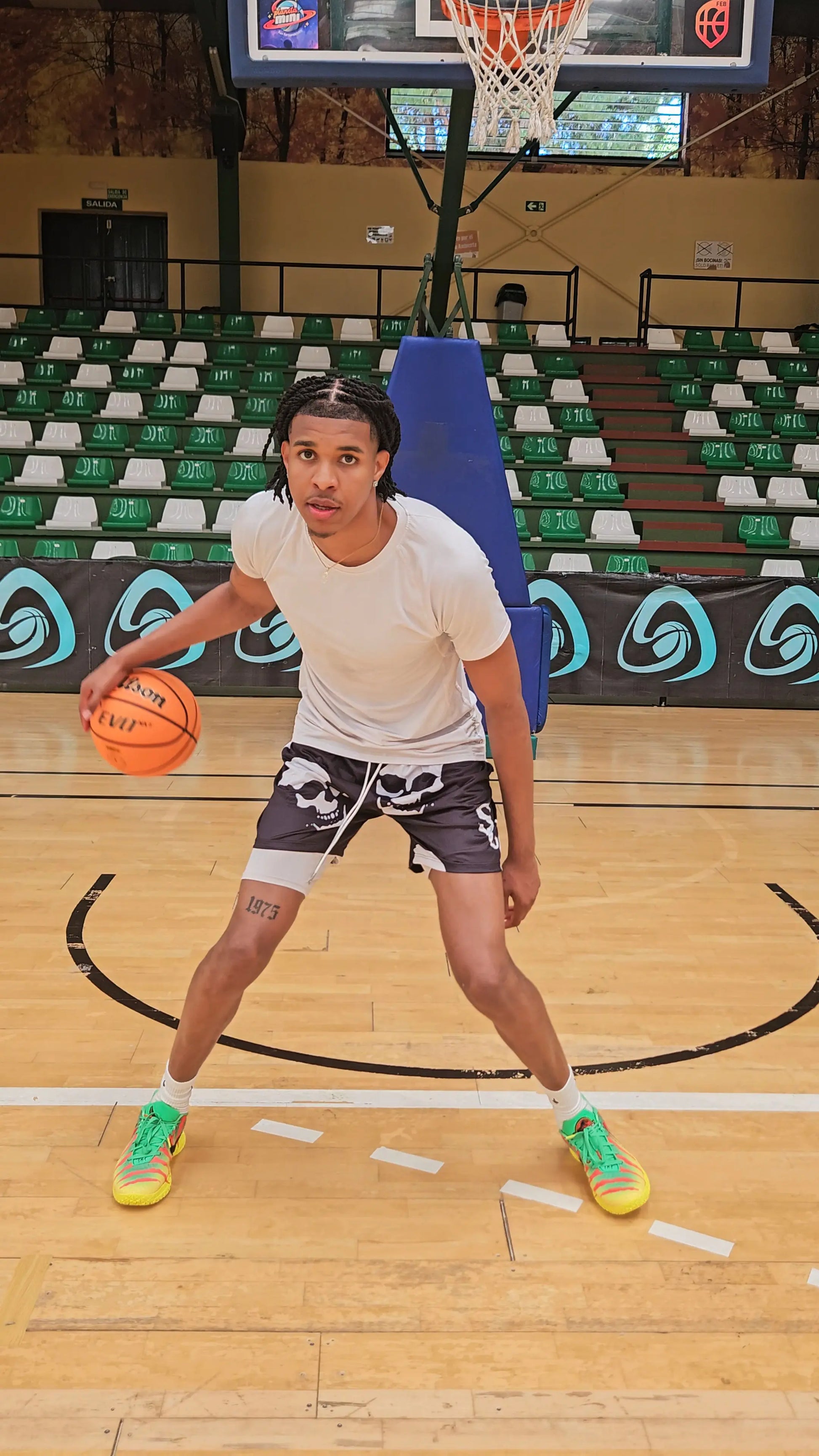 Basketball player dribbling a ball on an indoor court, wearing black basketball shorts with a white skull pattern