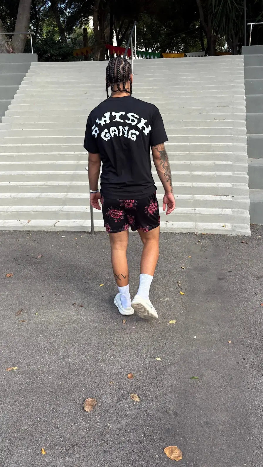 Back view of model wearing black SwishGang logo t-shirt outdoors, walking down steps – SwishGang