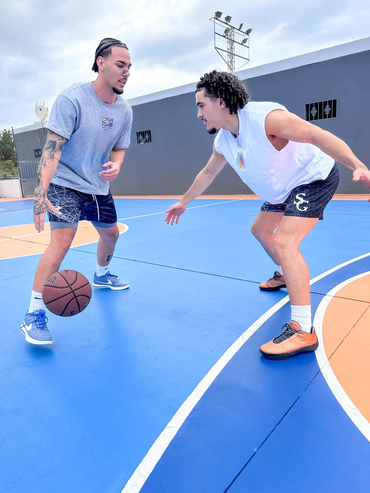 Players dribbling ball wearing black spider print basketball shorts on outdoor court – SwishGang