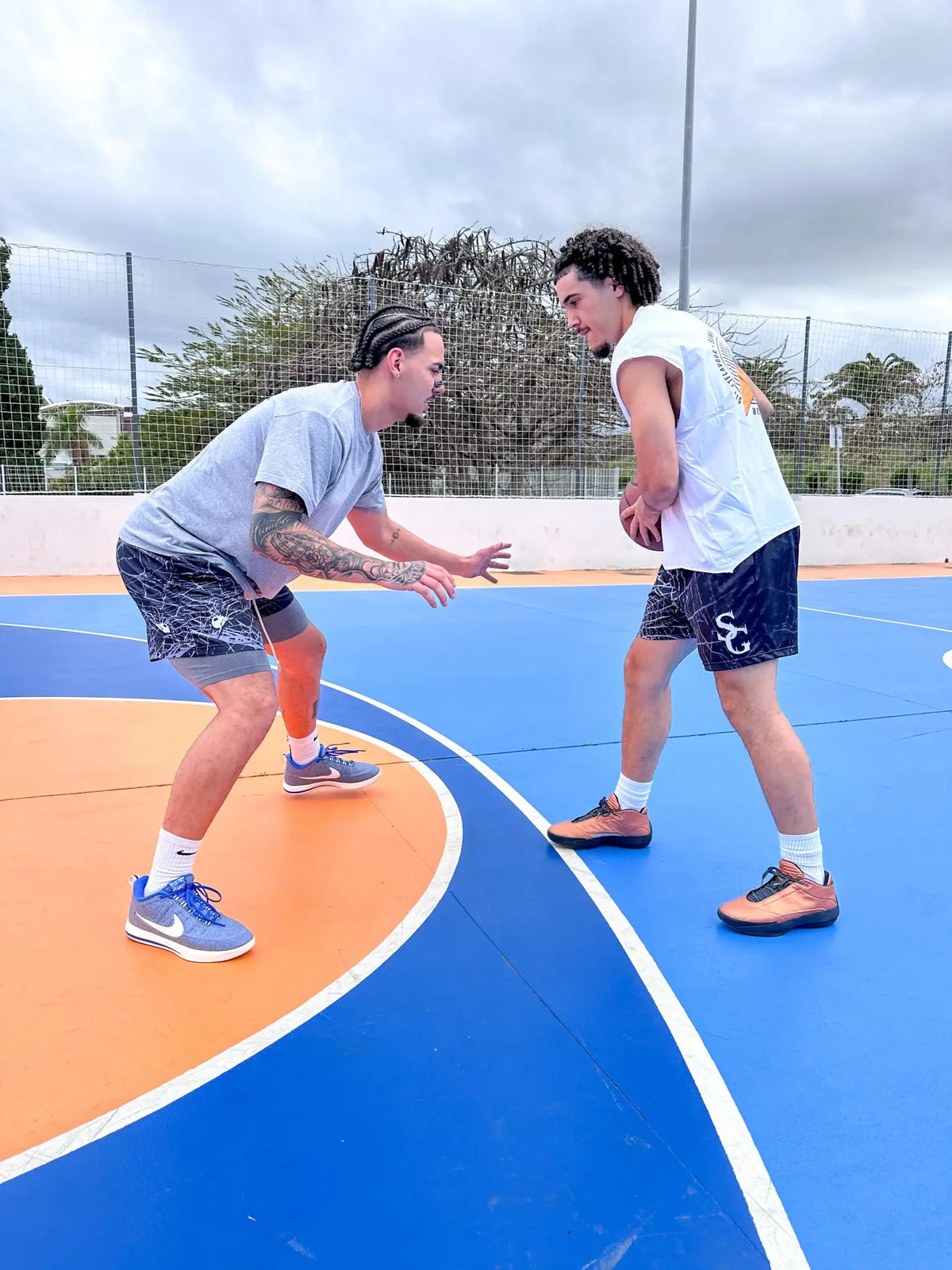 Two players in black spider print basketball shorts playing 1-on-1 on outdoor court – SwishGang