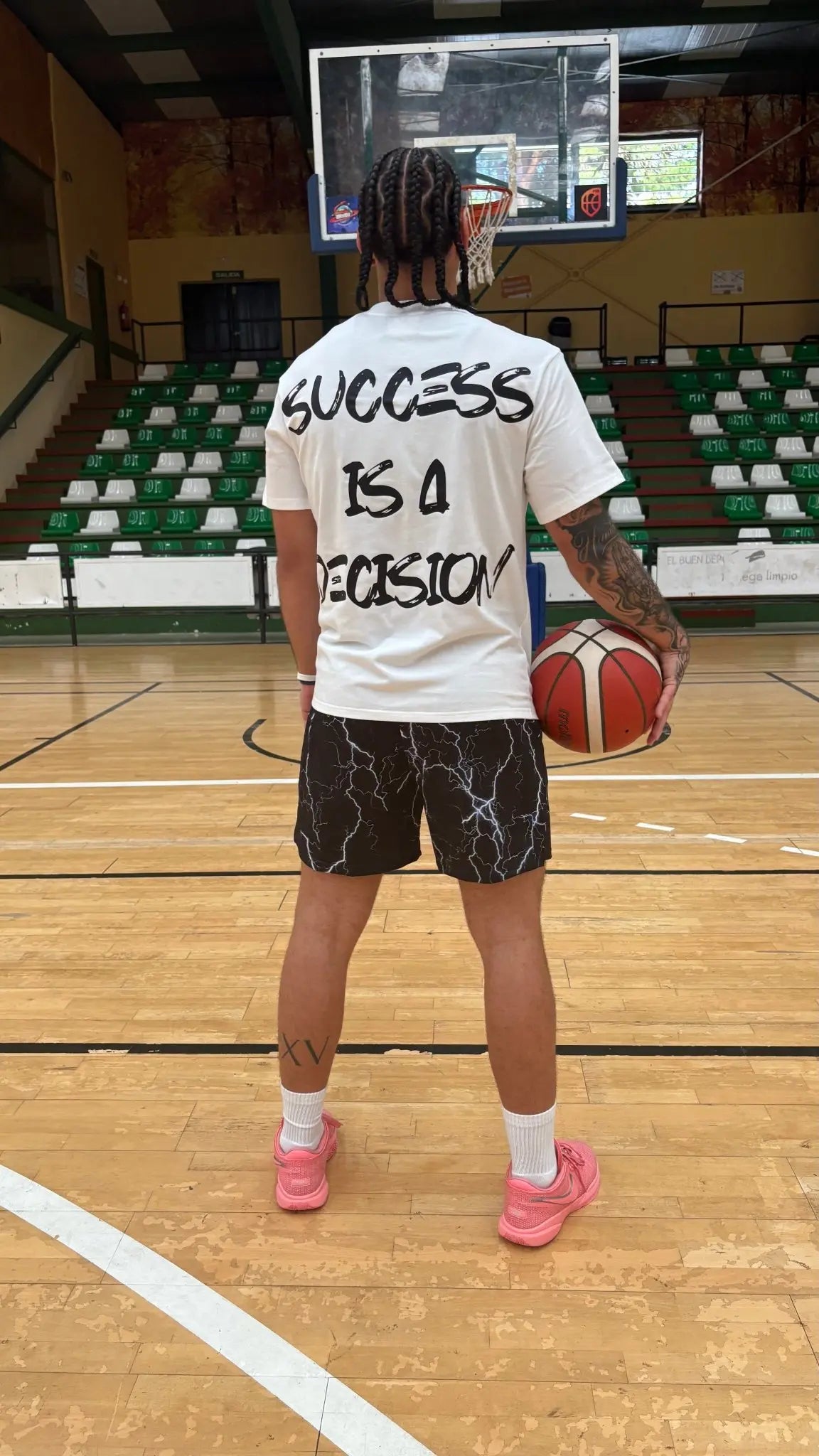 Back view of a basketball player wearing a white SwishGang t-shirt with the bold, hand-lettered "SUCCESS IS A DECISION" graphic on the back while on a basketball court