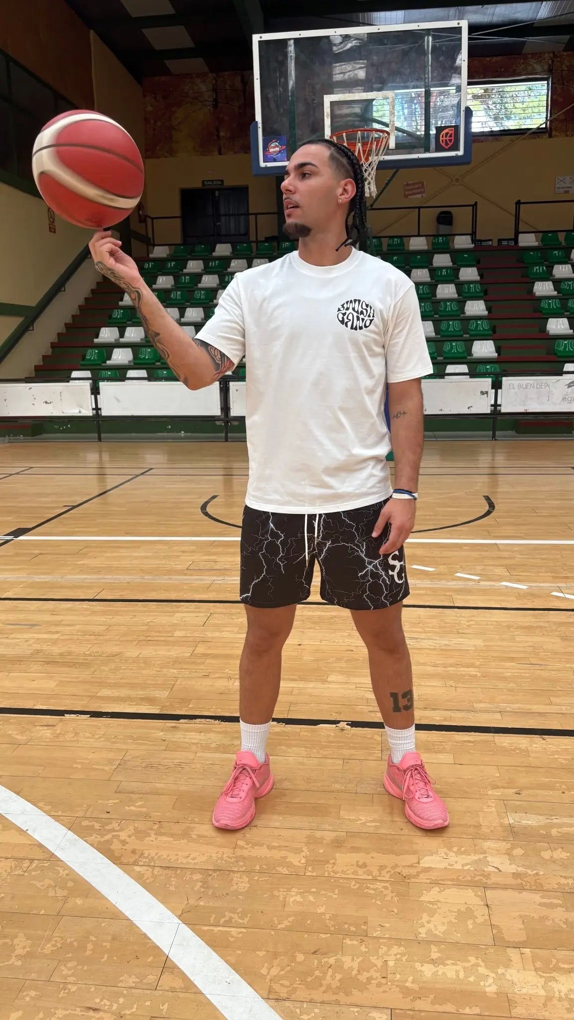 A basketball player spinning a basketball on his finger while wearing a white SwishGang "Success is a Decision" t-shirt on a basketball court