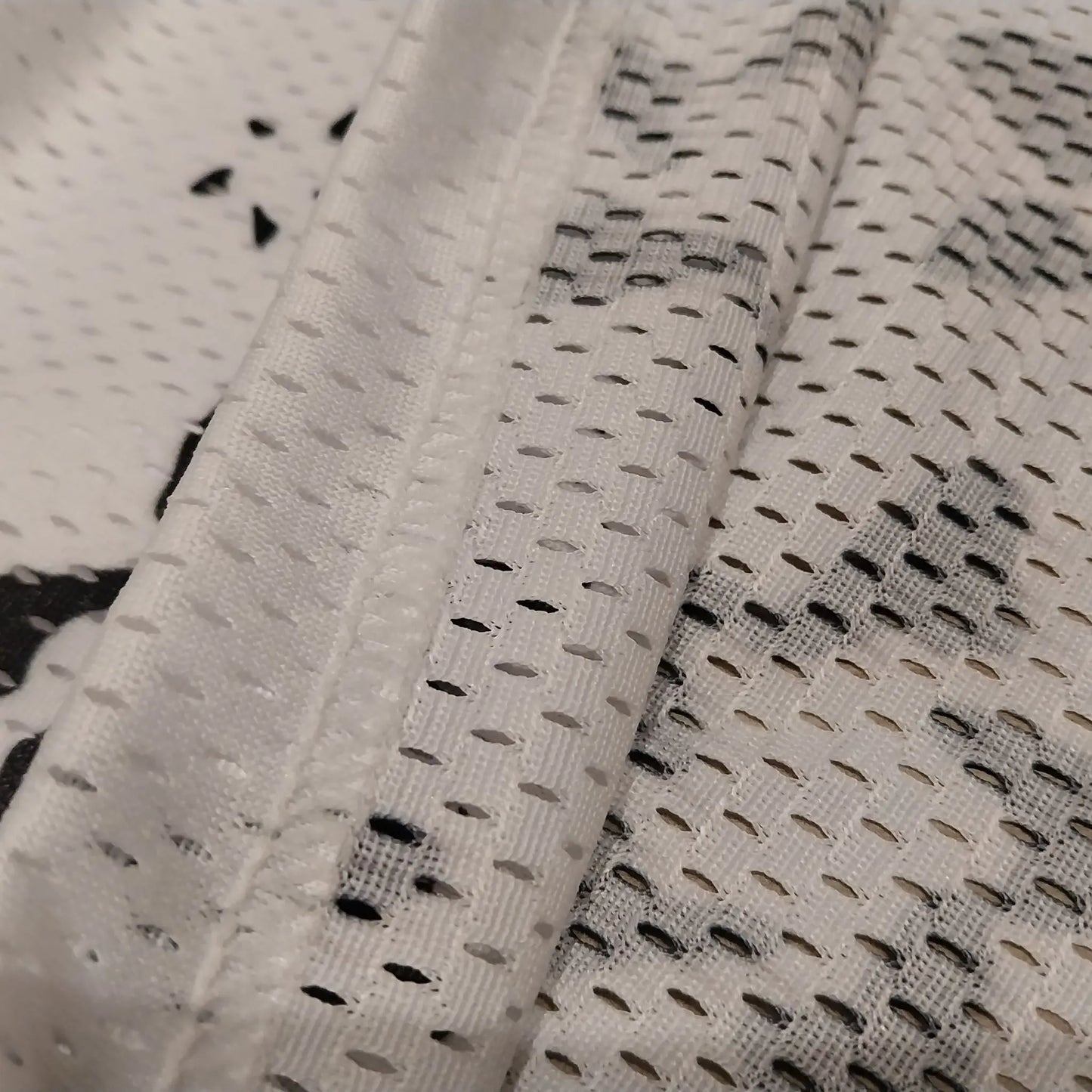 Close-up detail shot showcasing the breathable white mesh fabric texture and hem stitching of the basketball shorts