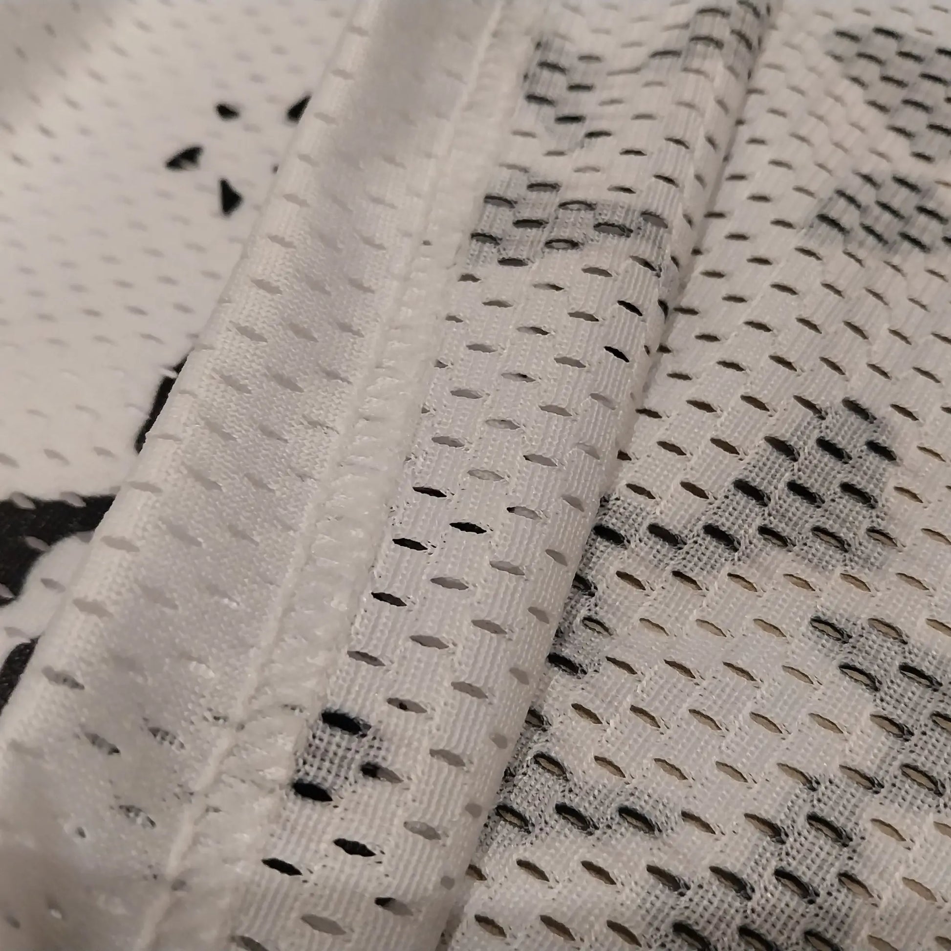 Close-up detail shot showcasing the breathable white mesh fabric texture and hem stitching of the basketball shorts