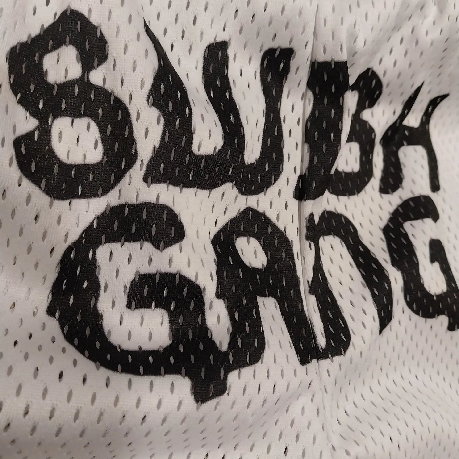 Close-up detail of the black SwishGang logo printed on the white mesh fabric of the basketball shorts