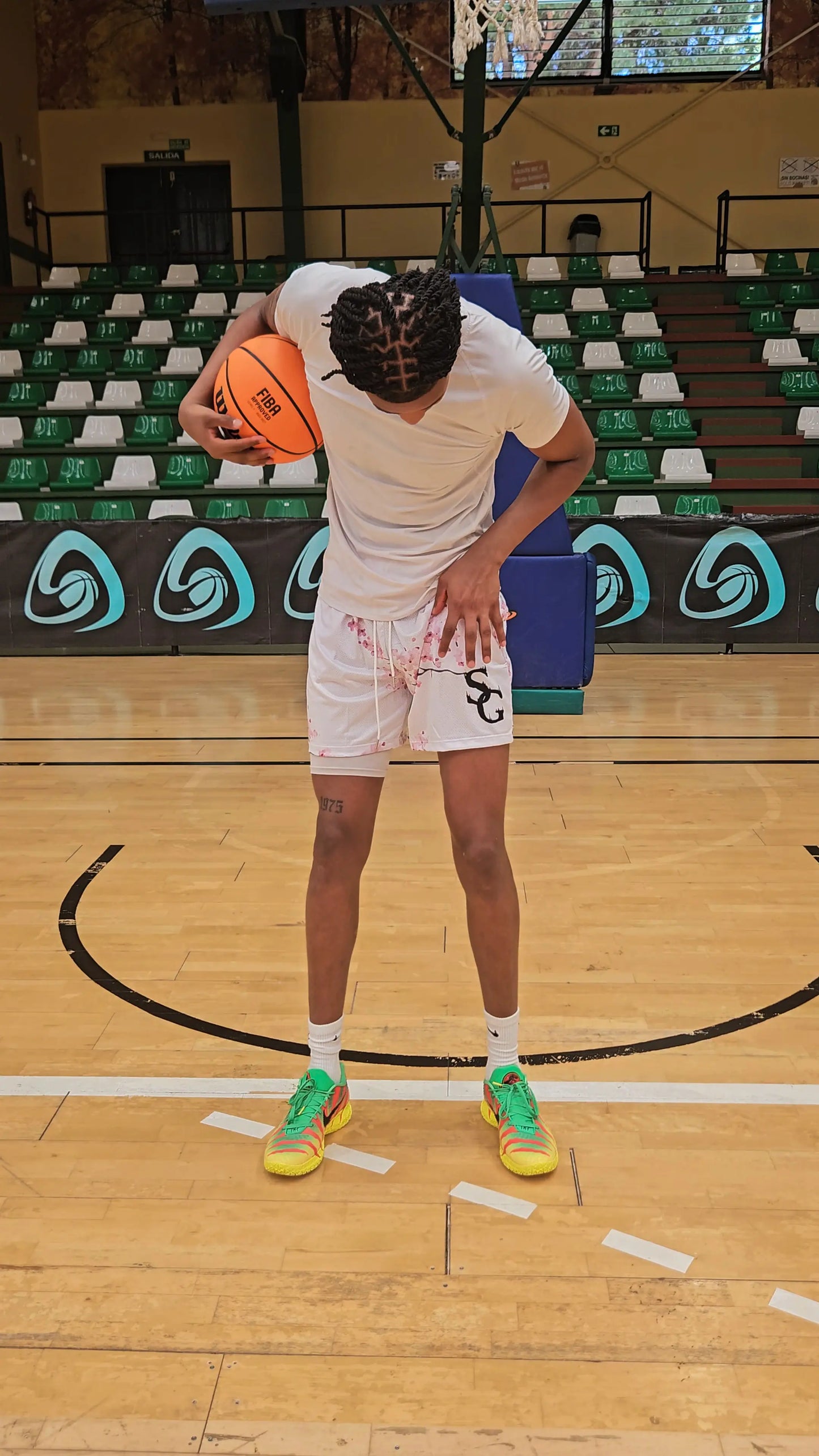 Full-body shot of a basketball player wearing white shorts with a cherry blossom design, holding a basketball on the court