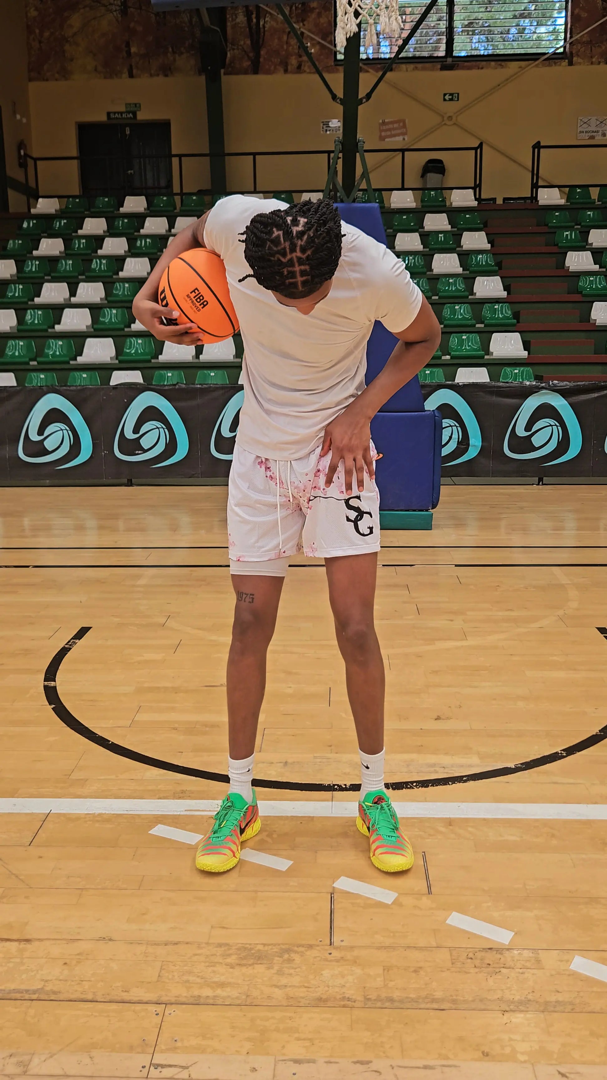 Full-body shot of a basketball player wearing white shorts with a cherry blossom design, holding a basketball on the court