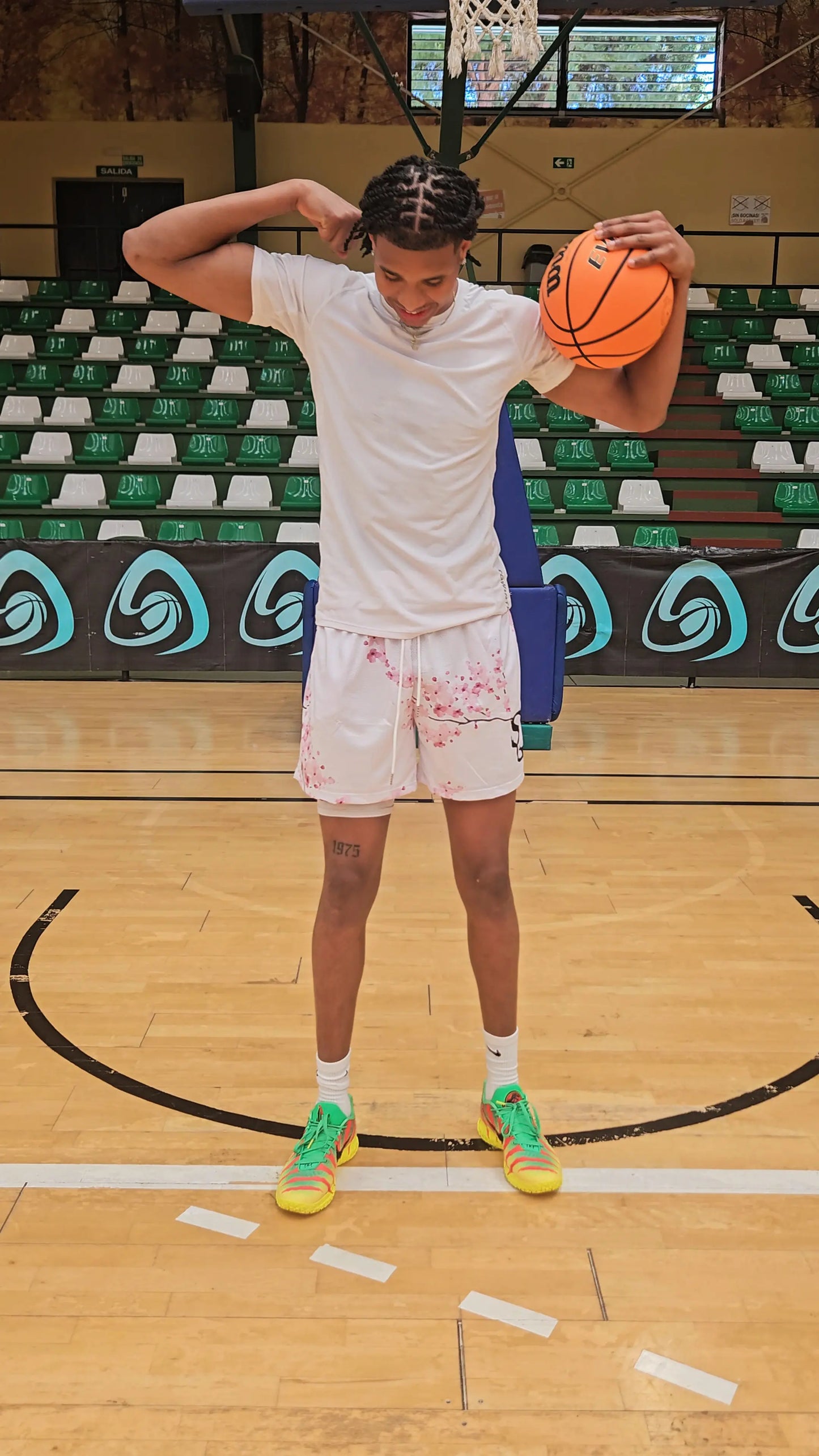 Athletic male model posing in white basketball shorts with a cherry blossom print on a basketball court