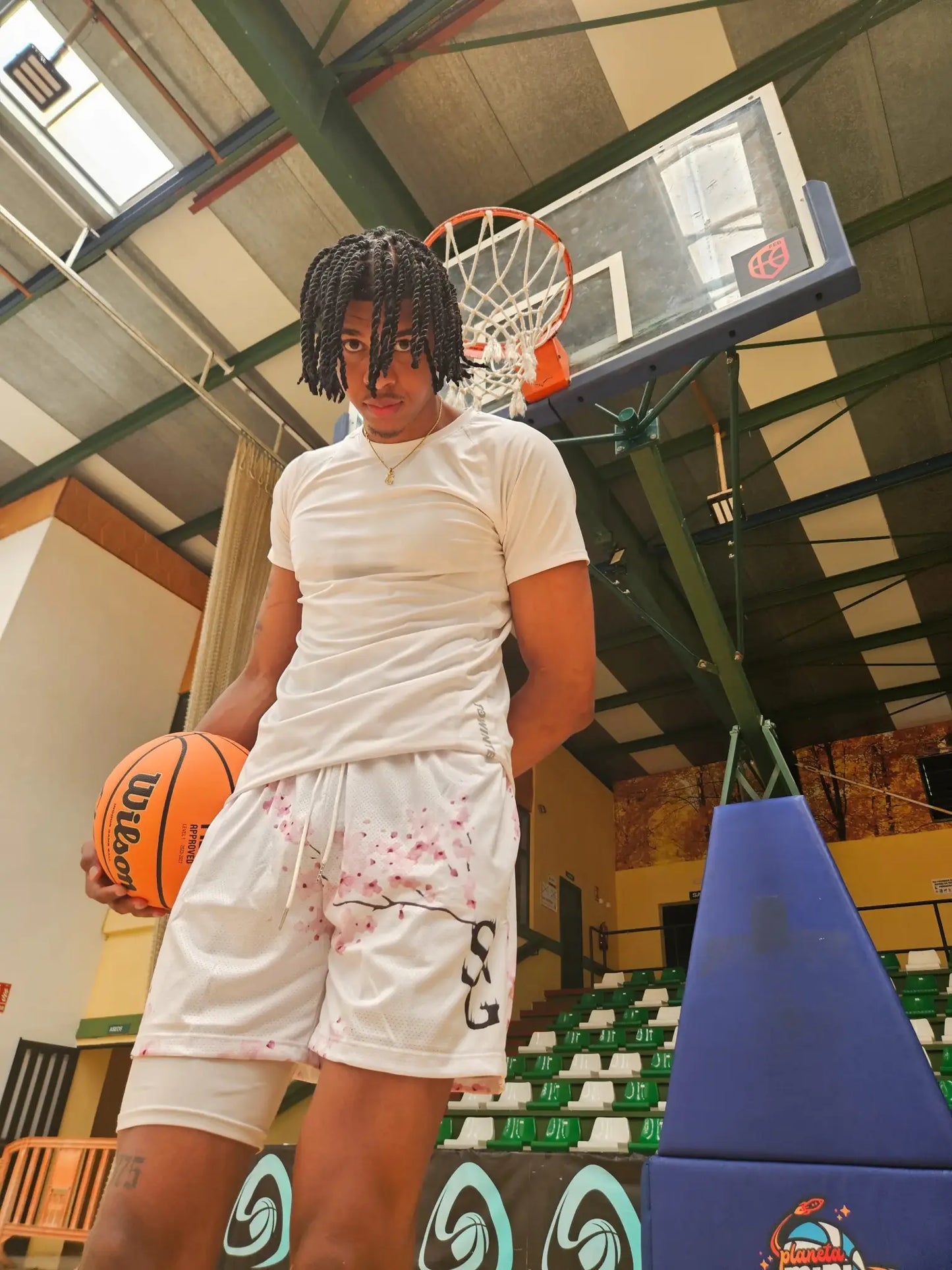 SwishGang model wearing white cherry blossom print basketball shorts, holding basketball on court